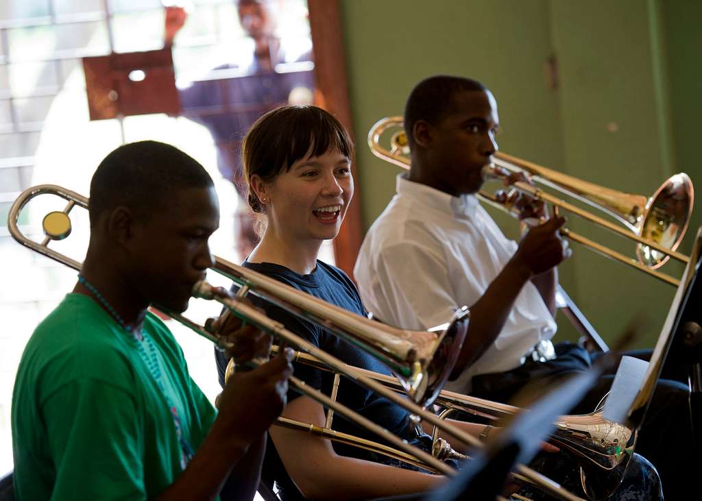 Three musicians sitting together with trombones.